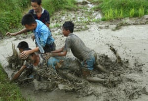 Kathmandu, Nepal. Students play in mud as they plant rice samplings on the field during National Paddy Day, also called Asar Pandra, that marks the commencement of rice crop planting
