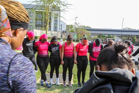 Women in pink and black running clothes stand together in a circle with heads bowed