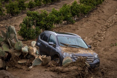 Un'auto che è stata spazzata via dalla strada sopra durante una frana giace in un frutteto l'11 gennaio 2023 vicino a Fillmore, in California.
