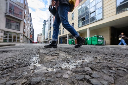 A pedestrian’s legs walking across Marsh street which is full of broken tarmac