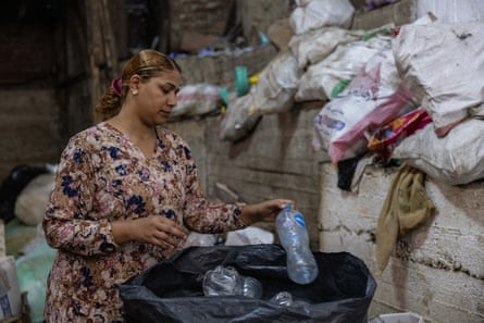 A woman in a flower print dress puts a plastic bottle in a black bag