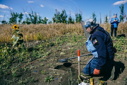 Olena Kabanova in protective gear kneeling and using a detector in a field.