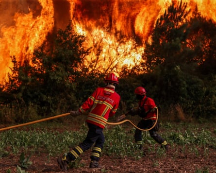 Firefighters hold a hose in front of flames