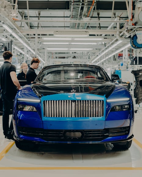 Workers inspect a nearly-completed blue Rolls-Royce Spectre on the factory assembly line