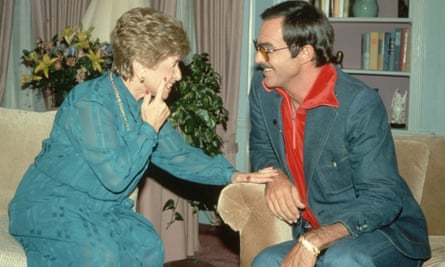 Dr Ruth Westheimer and Burt Reynolds chatting and laughing, Ruth leaning towards BR, touching his wrist with one hand and her cheek with the other