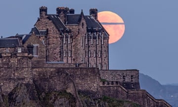 A pink full moon sets behind Edinburgh Castle.