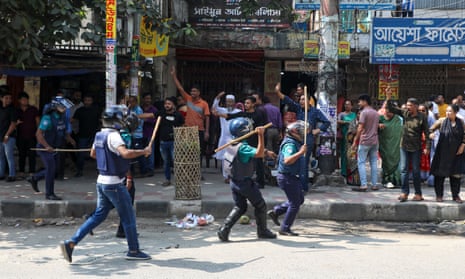 Police holding batons run towards a crowd of people standing by a roadside in Bangladesh