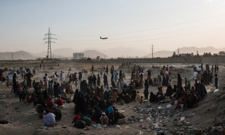 Hundreds of people camped in a dusty field near Kabul airport in August 2021 as a US military plane takes off in the background