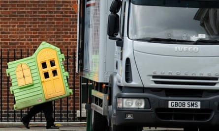 The front of a large, colourful plastic playhouse is carried to a waiting van
