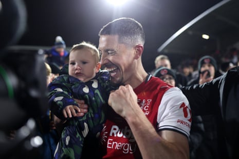 Ronan Coughlan holds his baby and pumps his fist, celebrating amid a crowd at night