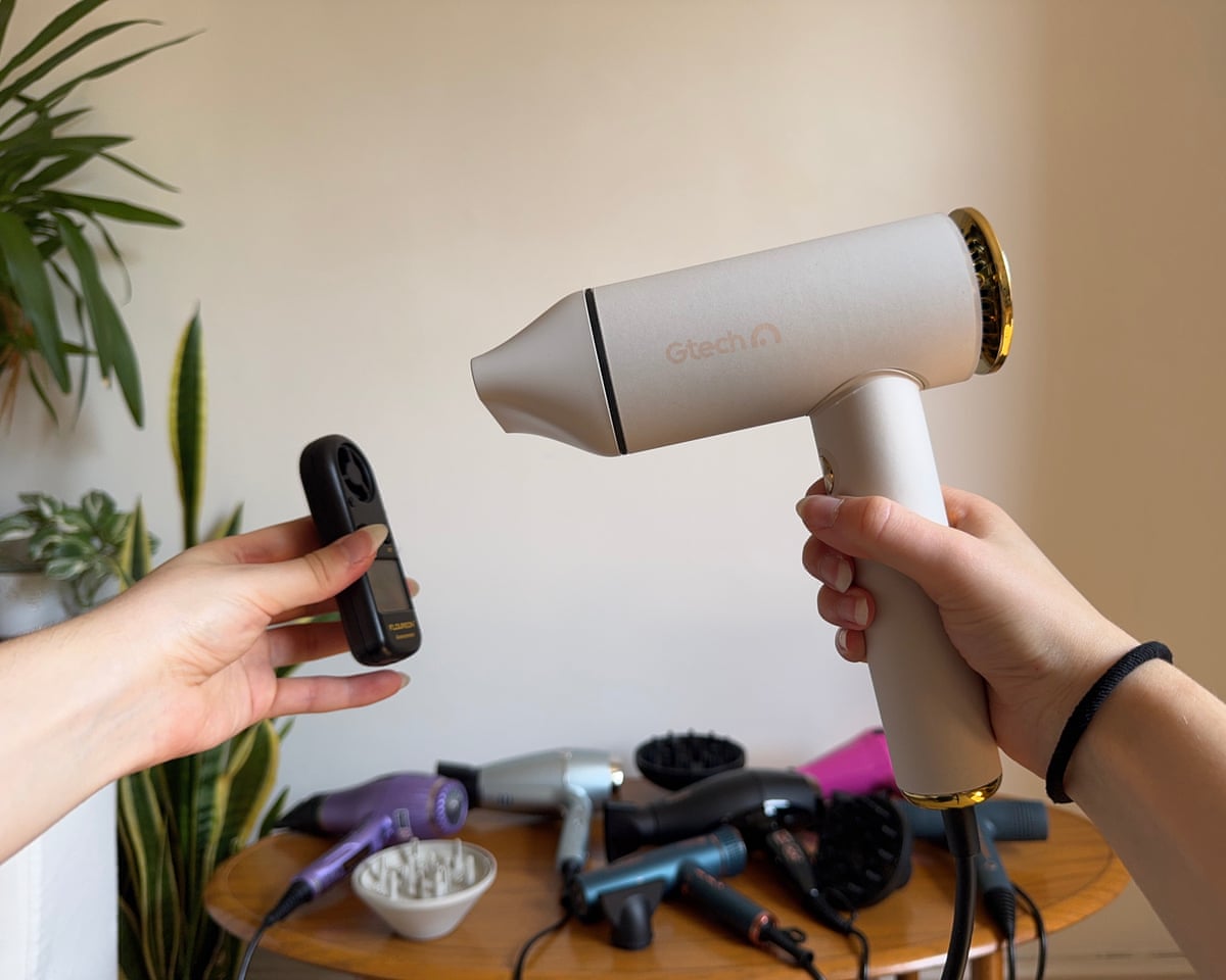 The right hand is in frame holding the hairdryer facing the testing device which is being held by the left hand.