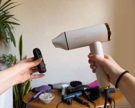 The right hand is in frame holding the hairdryer facing the testing device which is being held by the left hand.