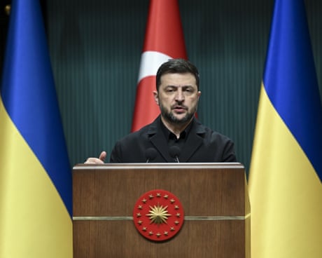 Volodymyr Zelenskyy speaks at a lectern flanked by Ukraine flags