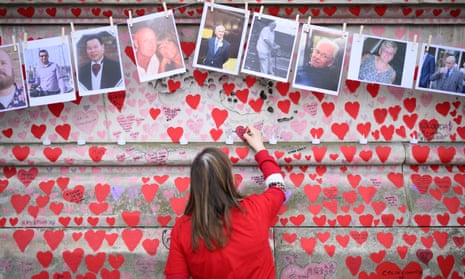 A woman leaves a message below photos of some of those who have died in the Covid-19 pandemic at the Covid memorial wall in London