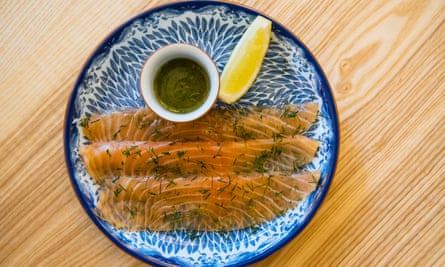 Three strips of pink gravadlax on a blue and white plate with a wedge of lemon