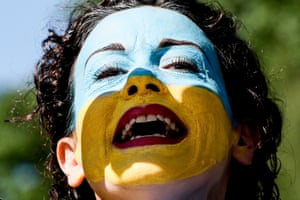 A woman wearing makeup in the colours of the Ukraine flag shouts
