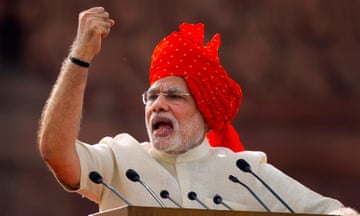 Narendra Modi addresses a crowd on Independence Day. He is looking towards the right and appears to be speaking, with one arm in the air. He is wearing a red turban and white kurta.