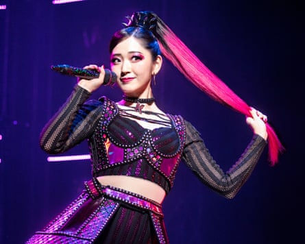 Airi Suzuki in a pink costume on stage, holding a microphone.