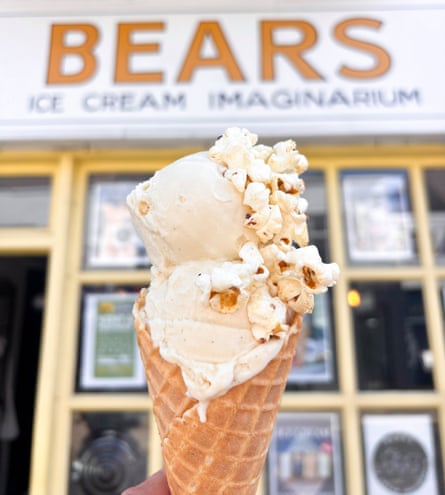 A waffle cone with two scoops of brown butter popcorn underneath signage of a Bears ice-cream shop