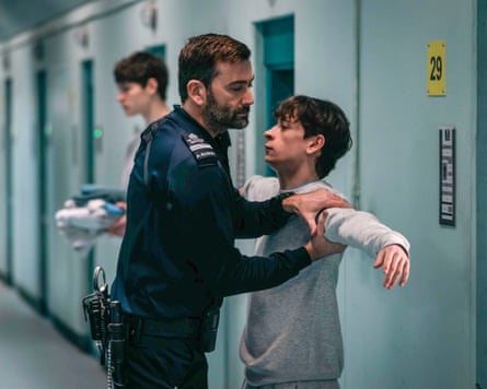 Tennant as a prison guard holding McCartney's arm, as if searching him