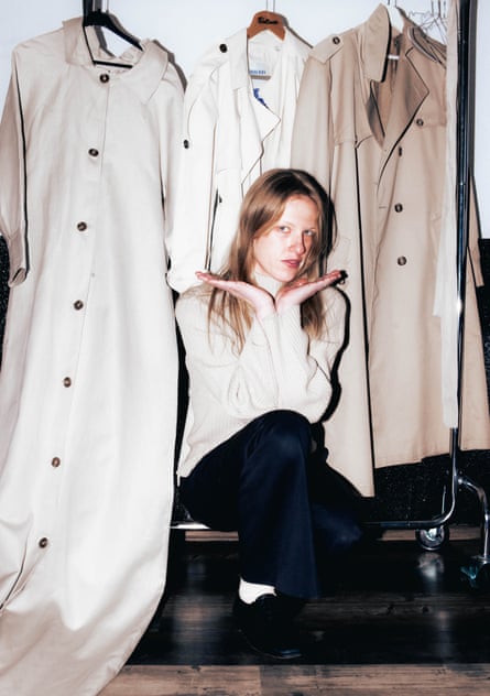 Three different-sized beige trenchcoats hung up behind Hobert sitting on a clothes rail