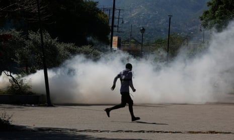 A man runs for cover as riot police launch tear gas in Port-au-Prince, Haiti