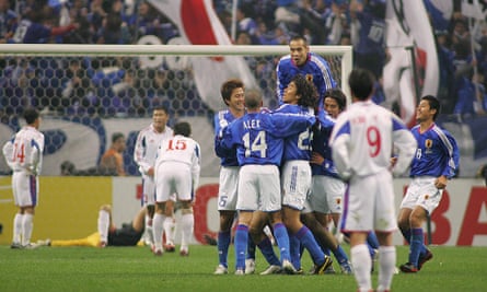 A group of Japan players in blue celebrate winning a match behind a white-shirted North Korean player with his hands on his hips