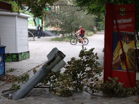 A local resident rides a bicycle past a fragment of a rocket embedded in the ground following a rocket attack in the town of Bakhmut on 12 August.