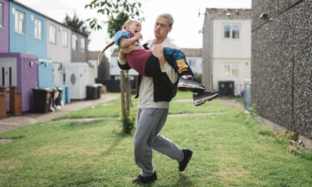 Harris Dickinson carrying Lola Campbell over a grassy area between houses