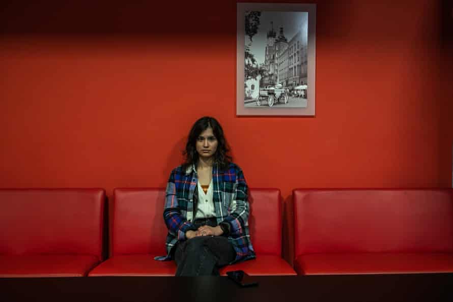 A woman sits on a row of red chairs against a red wall