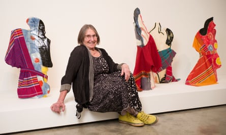A smiling woman with yellow shoes sits in front of colourful ceramic figures