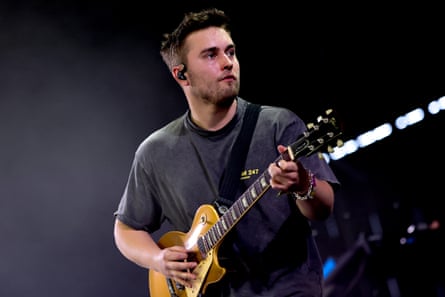 Sam Fender plays a guitar on stage.