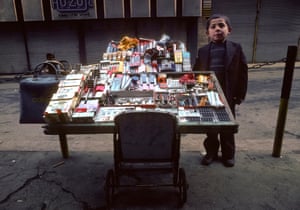 A child stands beside a street stall selling razor blades, shaving brushes, lighters and other small goods