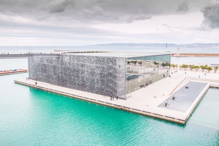 A modern rectangular building sitting on a white concrete base on turquoise water