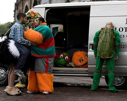 Riz Ahmed and other actors wearing costumes, standing beside a van