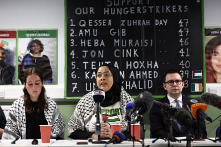Ella Moulsdale, Shahmina Alam and solicitor Daniel Cooper speak at a press conference; on a board is the names of the prisoners and their number of days on hunger strikes
