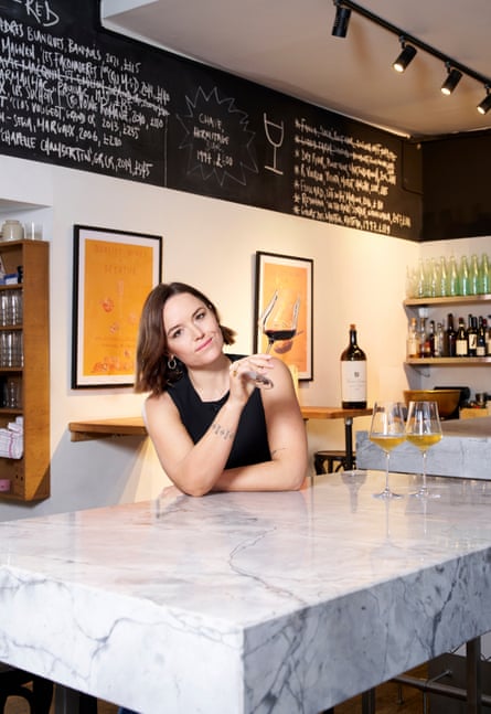 A woman with a long bob holds a glass of wine and sits behind a high marble counter in a wine bar