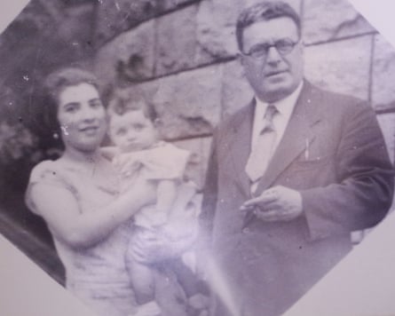 A faded black and white photo of a baby Gabriele in the arms of her young mother, standing beside her slightly older father wearing a suit and holding a cigarette