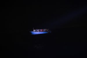 A group of migrants sit in a wooden boat during a search and rescue operation in the Mediterranean