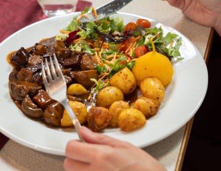 A person eating stew and potatoes and salad at a restaurant