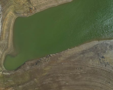 Aerial view of Ardingly Reservoir’s green water with exposed muddy shoreline from low capacity