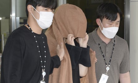 A woman whose face is completely covered by a brown jumper is escorted by two men, one either side of her who are wearing white face masks