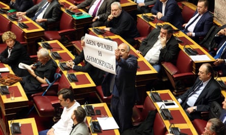 An MP holds a banner reading ‘Don’t blame Democracy’ in parliament.