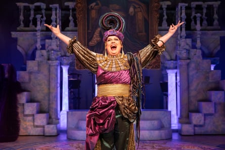 A theatre actor holds their hands wide and sings.