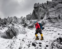 A woman in climbing gear standing in a desolate landscape of snow and jagged rocks