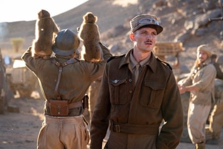 A man in military garb stands in a desert.