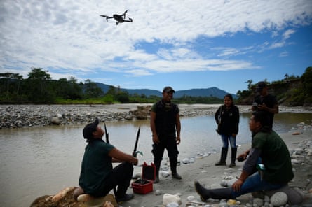 A group of Indigenous guards on a riverbank prepare to fly a drone for surveillance of the Aguarico River, Ecuador.