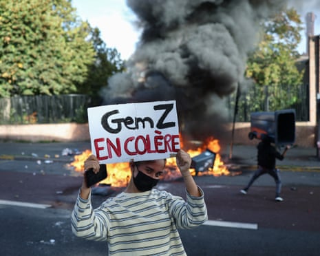 A student displays a placard which reads "Gen Z is Angry" near burning trash bins in Lille, northern France.