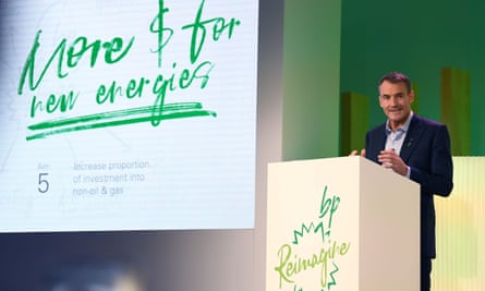 Looney at a podium speaking next to a large display saying ‘More $ for new energies’