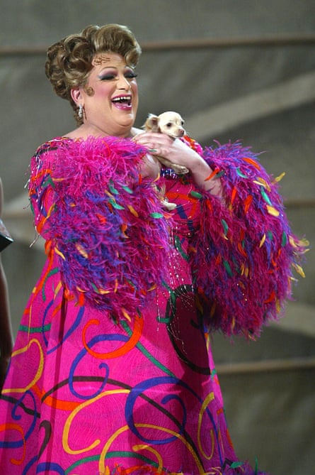Fierstein in drag holding a miniature dog and wearing a colourful pink dress